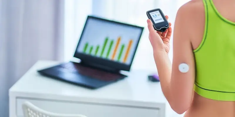 Woman checking glucose monitor with laptop displaying charts