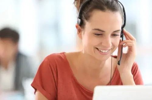 Woman with headset smiling at computer screen